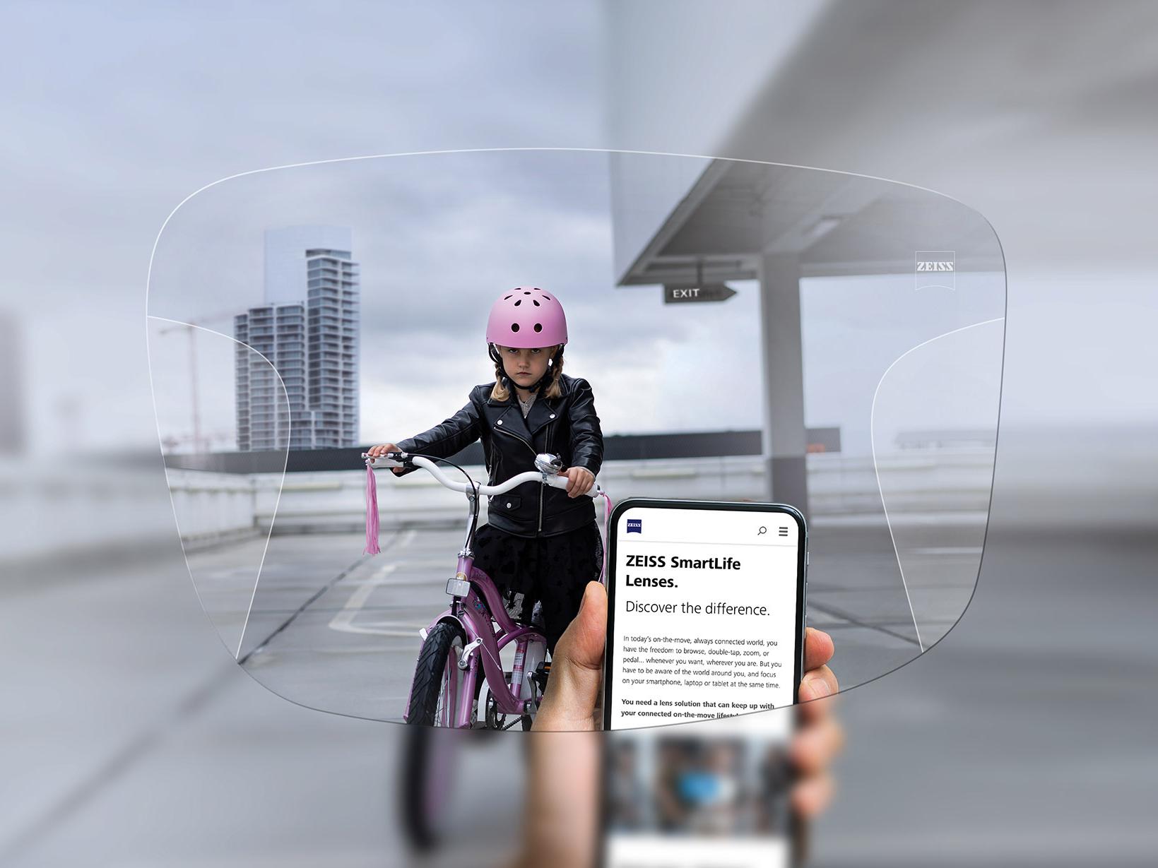 Henkilö katsoo puhelintaan ZEISS SmartLife Progressive -linssien läpi. Taustalla näkyy pyöräilevä tyttö, jolla on vaaleanpunainen kypärä. 