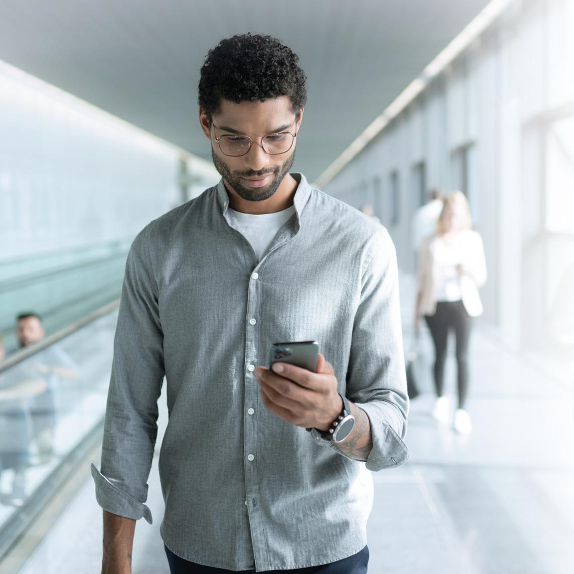 Nuori ZEISS SmartLife -linssejä käyttävä mies katsoo puhelintaan kävellessään.