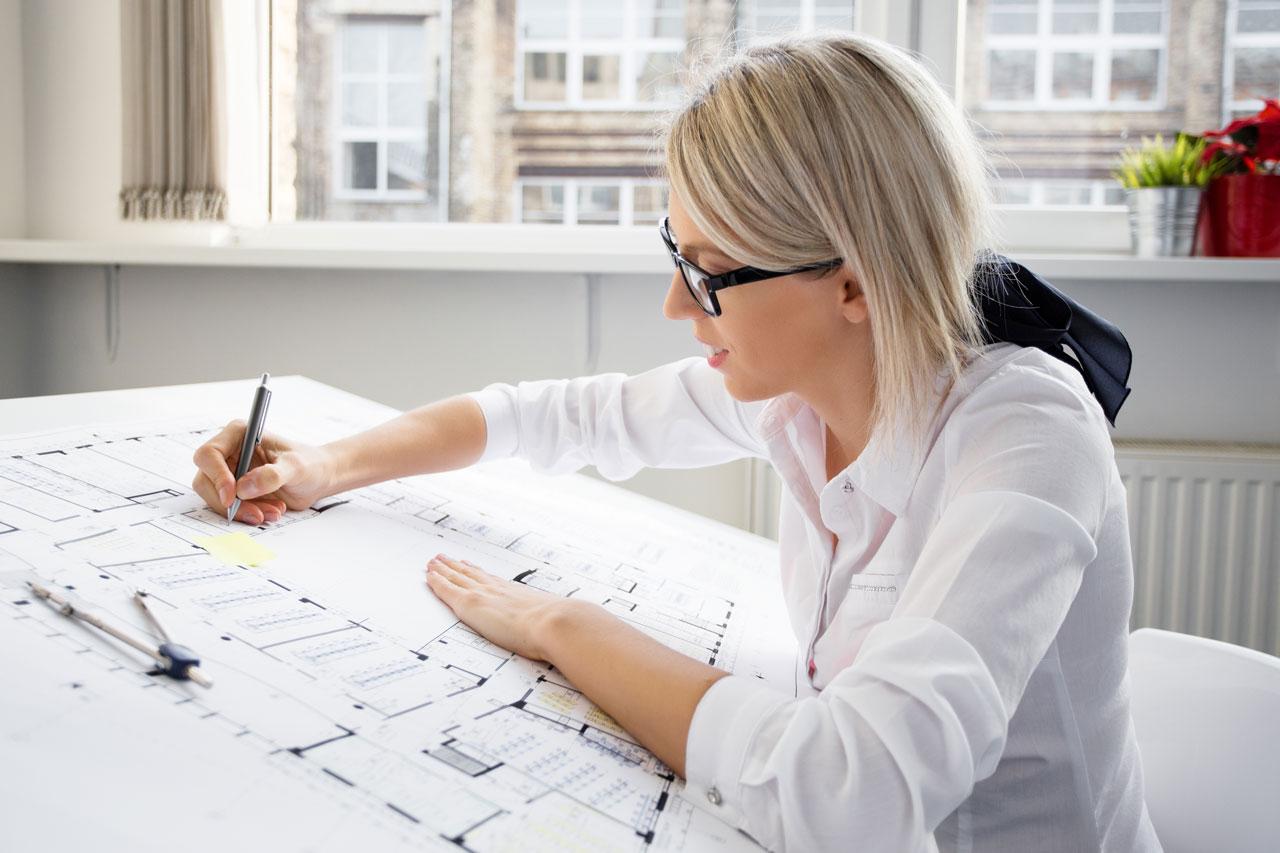 Nuori naispuolinen ja silmälasipäinen arkkitehti työskentelee suunnitelman parissa