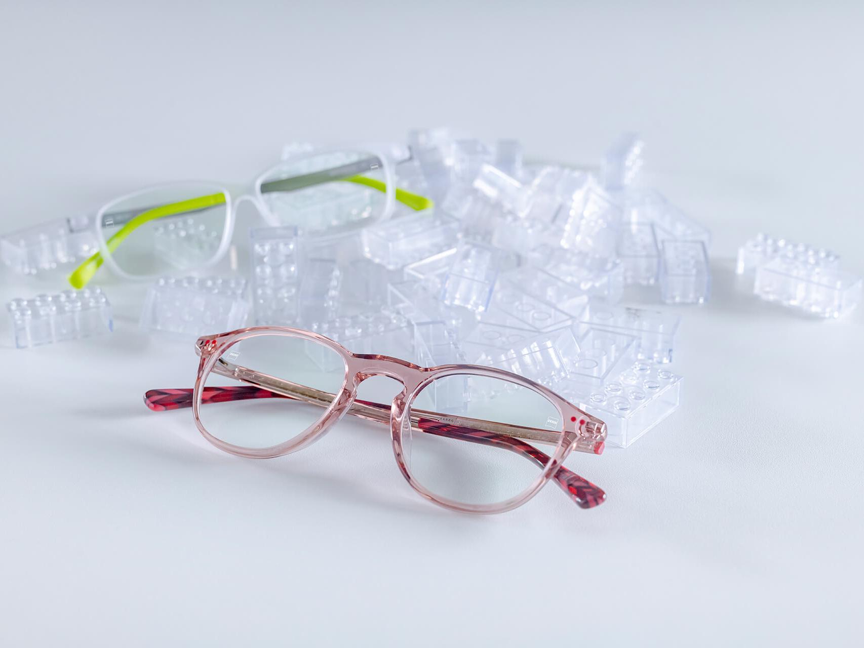 Kahdet lasten silmälasit, joissa on ZEISS-linssit ja DuraVision® Kids -pinnoite. Silmälasit on sijoitettu läpinäkyvien lasten palikoiden keskelle.