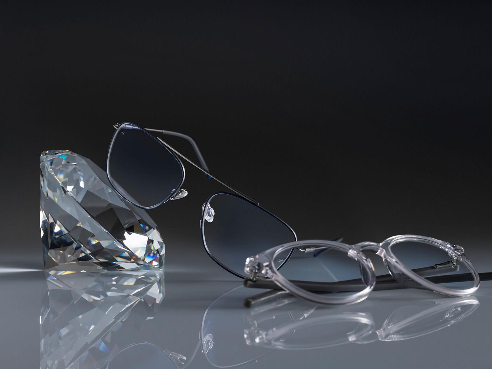 Kahdet ZEISS-linsseillä varustetut silmälasit, joissa on kaikkien aikojen kovin ZEISS-pinnoite – DuraVision® Platinum. Toiset silmälasit nojaavat kristallia vasten, toiset on asetettu sangat taitettuna alustaa vasten. Molemmissa on kirkkaat linssit ilman sinertävää heijastusta.
