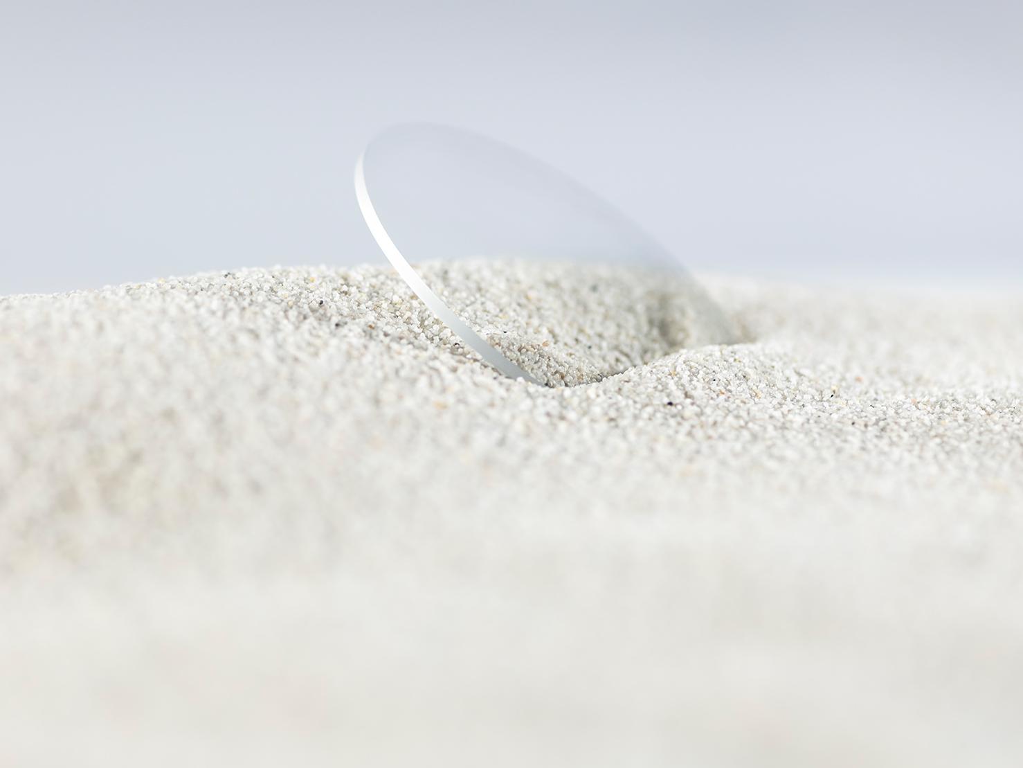 Kestävällä pinnoitteella pinnoitettu ZEISS-linssi on peitetty karkeaan hiekkaan mutta on silti naarmuton.