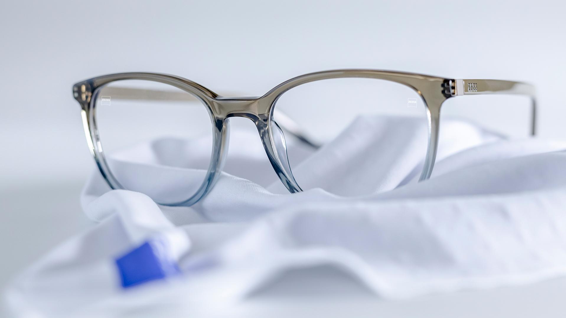 Valkoisen mikrokuituliinan päällä on silmälasit, joissa on siniharmaat kehykset ja ZEISS-linssit DuraVision®-pinnoitteella.